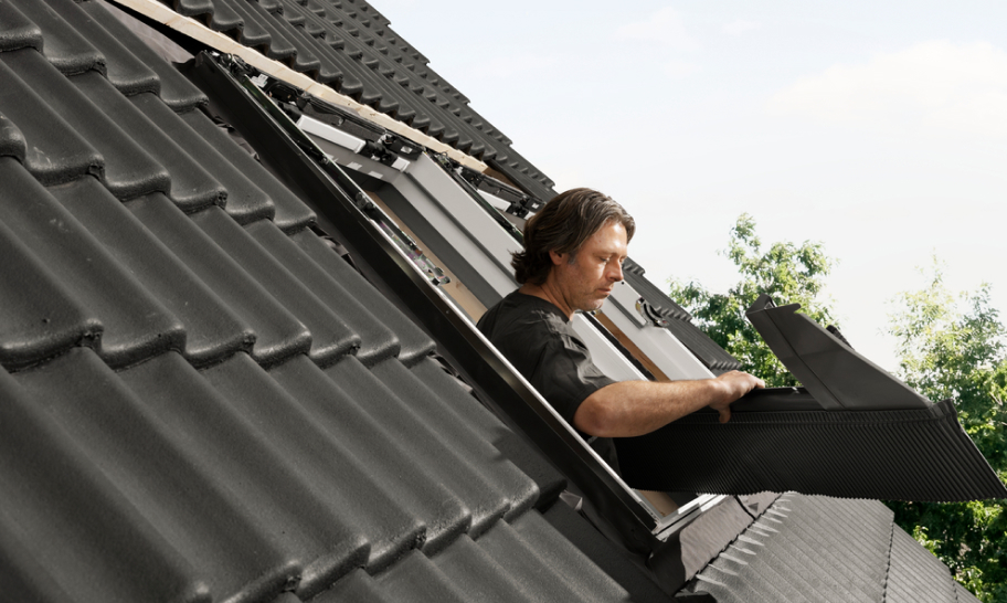 Installer installing a new VELUX roof window on a roof with black tiles.