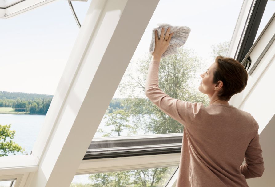 Woman cleaning her VELUX roof window from the inside in her living room.