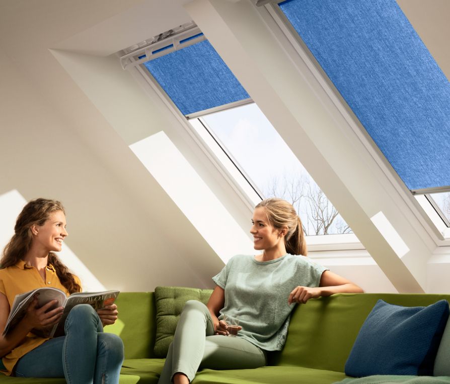 Two woman talking in the couch with two VELUX roof windows behind them, which have two blue VELUX awning blinds.