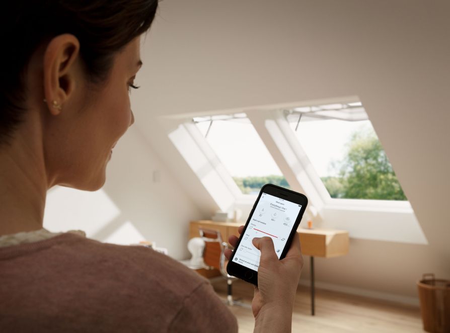 Woman controlling her two VELUX roof windows with the VELUX ACTIVE app on her smartphone.