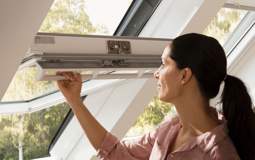Woman ventelitating her room by opening her VELUX roof window.