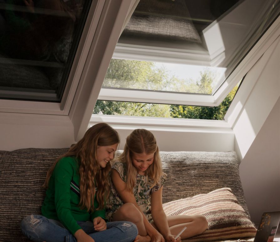 Two girls sitting in a  kids room with two VELUX roof windows behind them, which have VELUX blackout blinds.