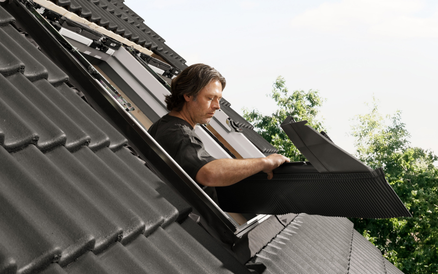 Installer installing a new VELUX roof window on a roof with black tiles.