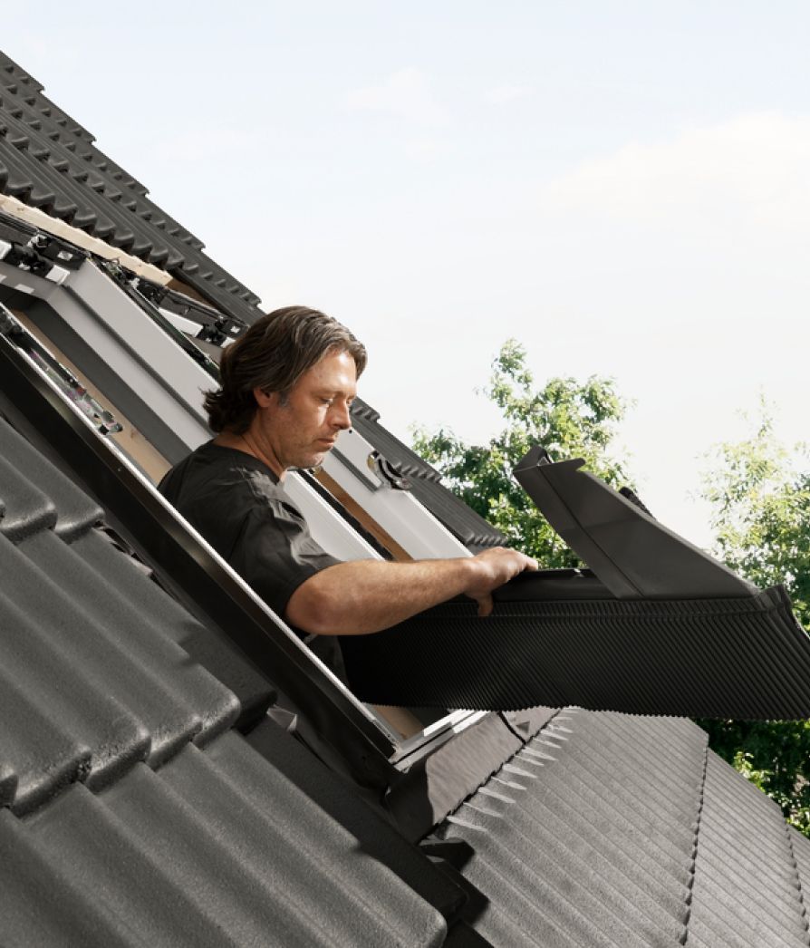 Installer installing a new VELUX roof window on a roof with black tiles.