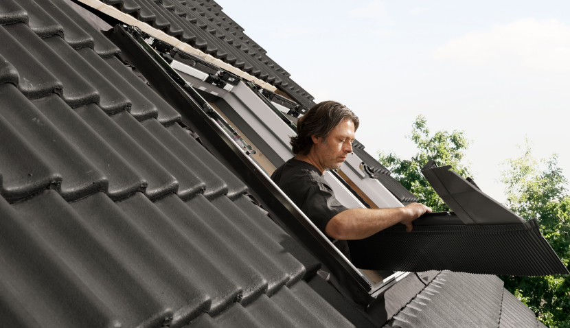 Installer installing a new VELUX roof window on a roof with black tiles.