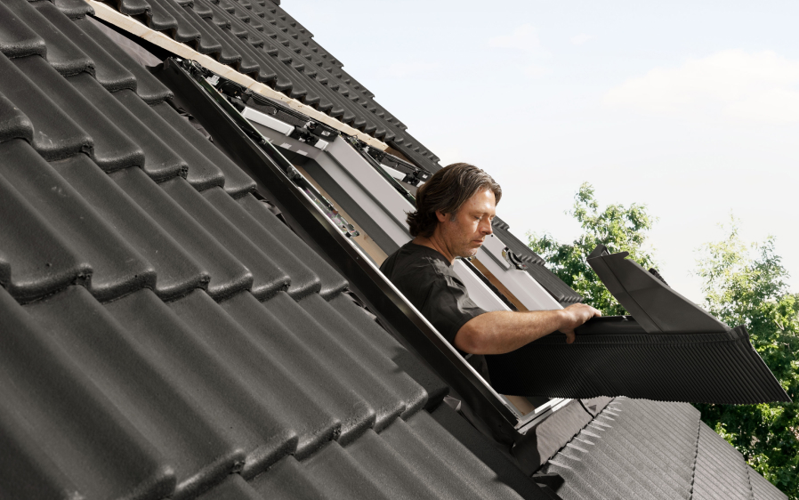 Installer installing a new VELUX roof window on a roof with black tiles.