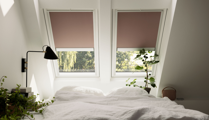 Bright, white painted bedroom with two VELUX roof windows, which have purple VELUX blackout blinds. 