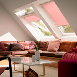 Image of two roof windows with light pink blinds installed above a couch