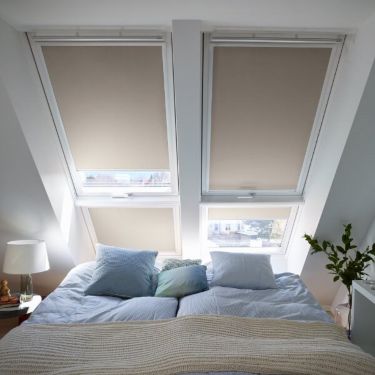 There are four VELUX roof windows above a bed. Each window is covered by a beige Blackout blind.