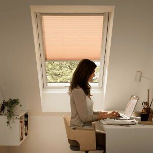 Woman working at a desk beside a VELUX roof window with pink blind