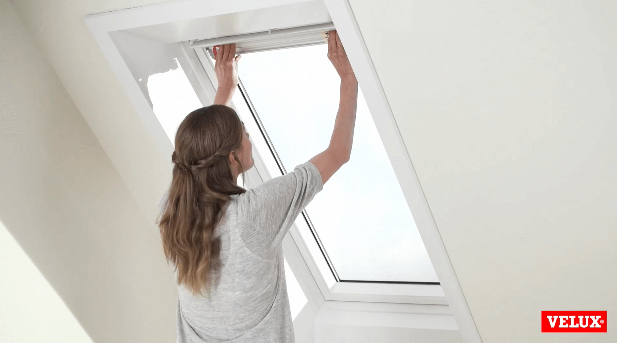 A woman is installing a VELUX blind to her VELUX roof window. 