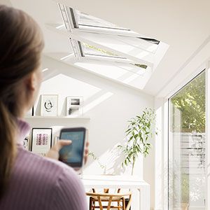 Image of a woman in her living room controlling her roof windows with her smartphone