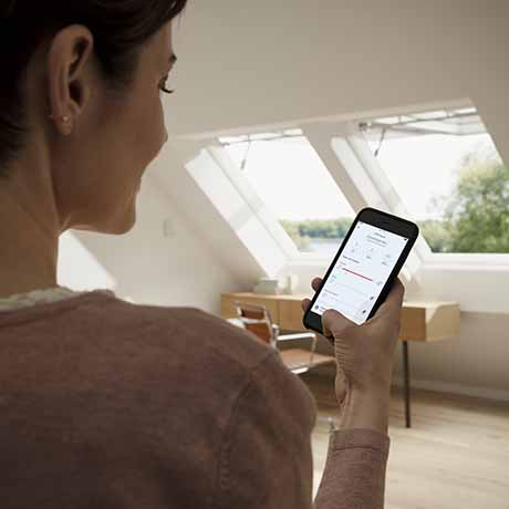 image of woman using a smart phone to operate electric VELUX roof windows
