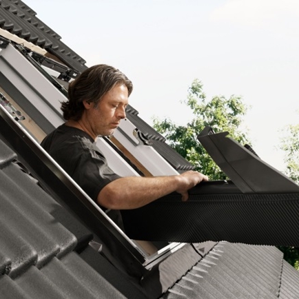 Installer installing a new VELUX roof window on a roof with black tiles.